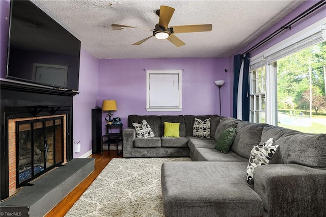 living room featuring a ceiling fan, a textured ceiling, a fireplace with raised hearth, and wood finished floors