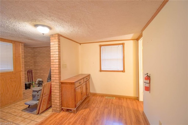 corridor with baseboards, light wood-type flooring, a textured ceiling, and visible vents