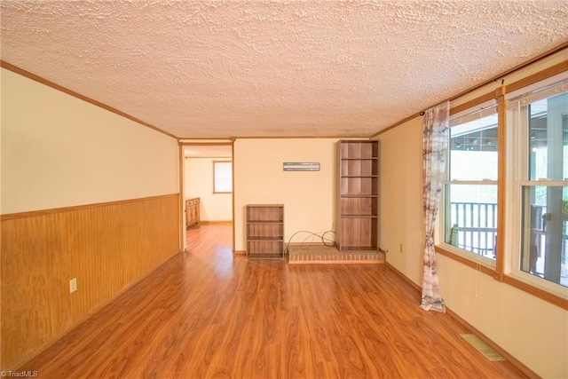 empty room featuring crown molding, a textured ceiling, wainscoting, and wood finished floors