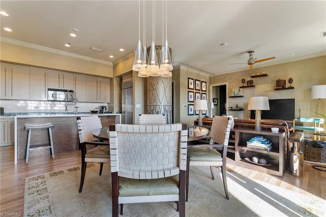 dining area featuring light wood-type flooring, sink, ornamental molding, and ceiling fan with notable chandelier