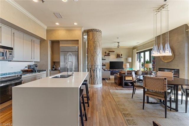 kitchen featuring stainless steel appliances, white cabinets, a kitchen island with sink, pendant lighting, and light wood-type flooring