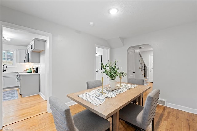 dining space featuring light wood-type flooring, arched walkways, baseboards, and visible vents