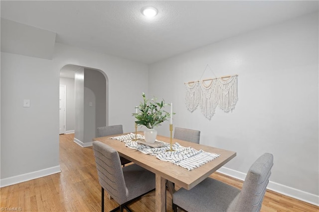 dining area featuring arched walkways, baseboards, and light wood-type flooring