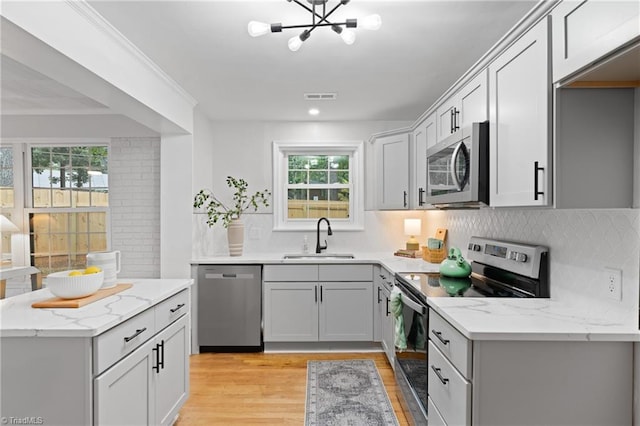 kitchen with backsplash, a sink, light stone countertops, stainless steel appliances, and light wood-style floors