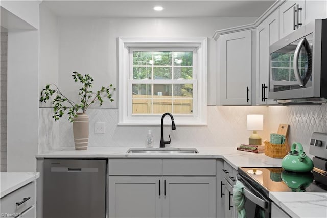 kitchen featuring decorative backsplash, stainless steel appliances, recessed lighting, a sink, and light stone counters