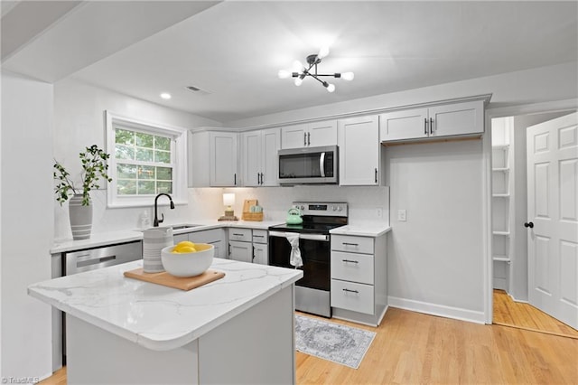 kitchen with light wood-type flooring, stainless steel appliances, a kitchen island, a sink, and light stone countertops