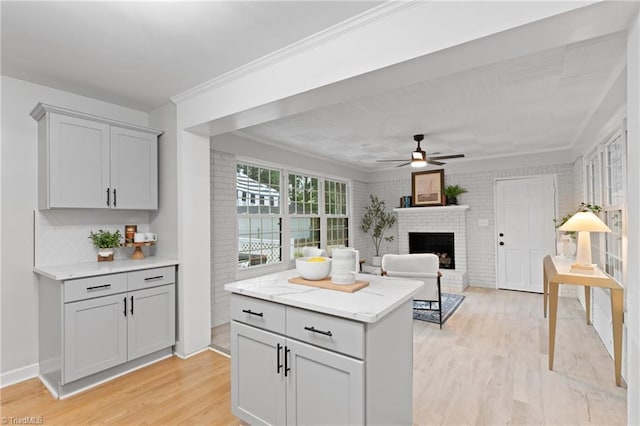 kitchen featuring gray cabinetry, light wood-type flooring, ceiling fan, and a brick fireplace