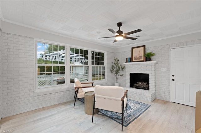 living area featuring a ceiling fan, a fireplace, wood finished floors, brick wall, and ornamental molding