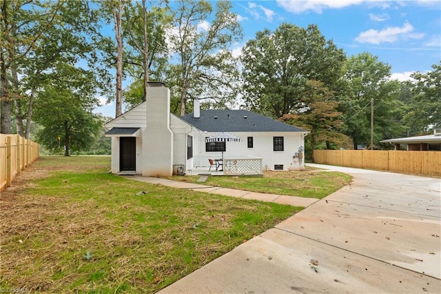 back of house featuring driveway, a chimney, a yard, and fence private yard