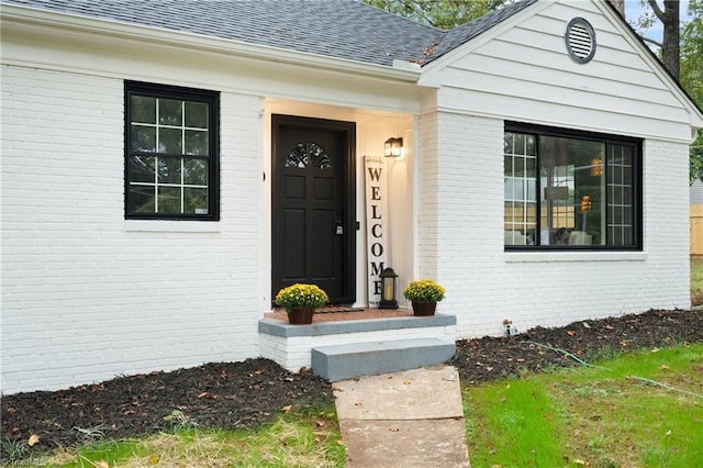 entrance to property featuring a shingled roof and brick siding