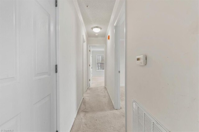 corridor with light colored carpet, a textured ceiling, and ornamental molding