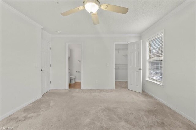 unfurnished bedroom featuring a walk in closet, ensuite bath, ornamental molding, light colored carpet, and ceiling fan