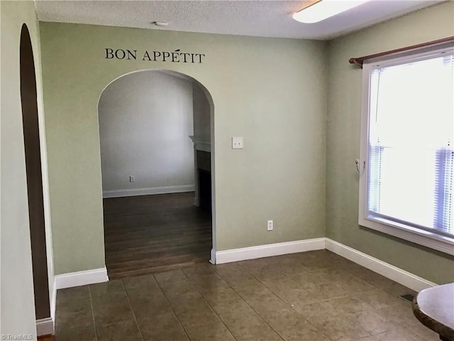 unfurnished room featuring tile patterned flooring, baseboards, arched walkways, and a textured ceiling