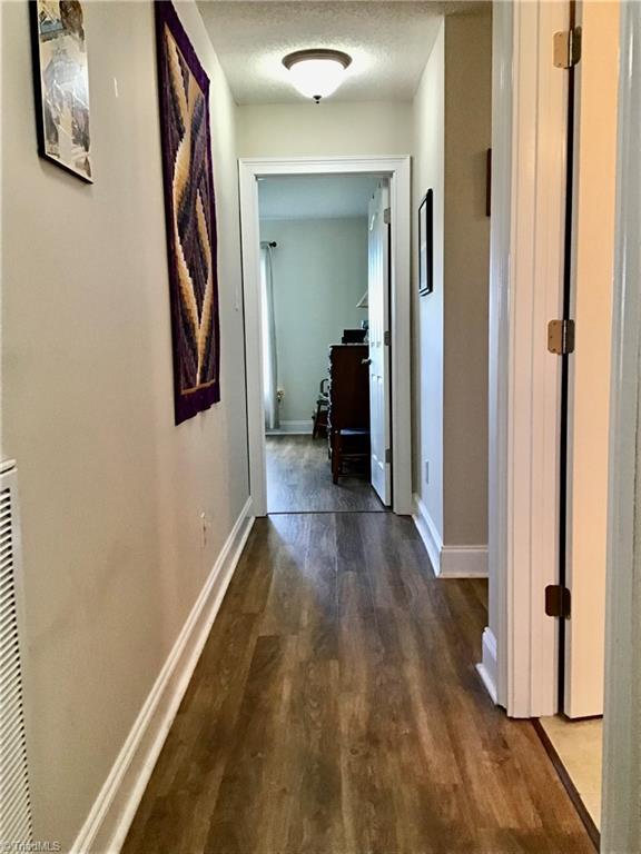 hallway featuring baseboards, dark wood finished floors, and a textured ceiling