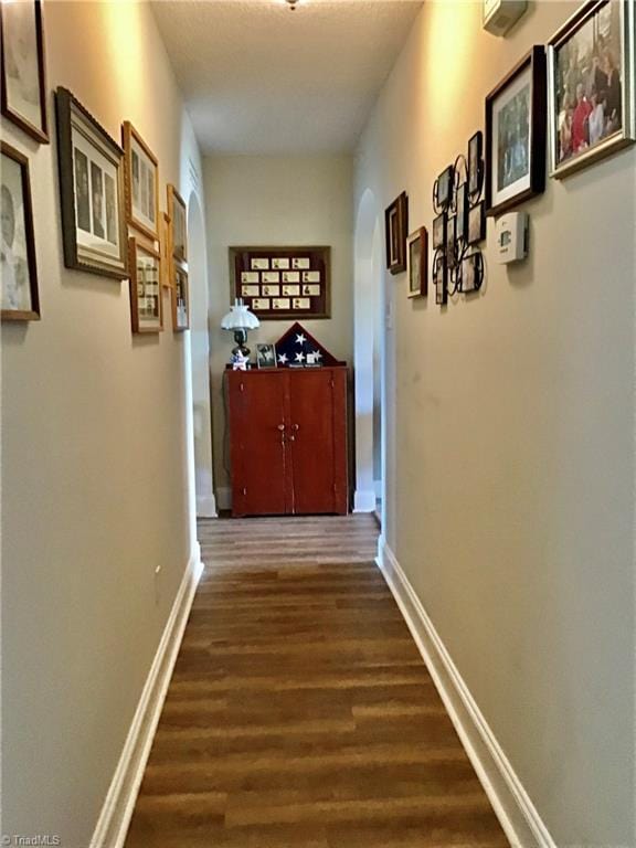 hallway with dark wood-type flooring, arched walkways, and baseboards