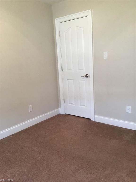 spare room featuring baseboards and dark carpet