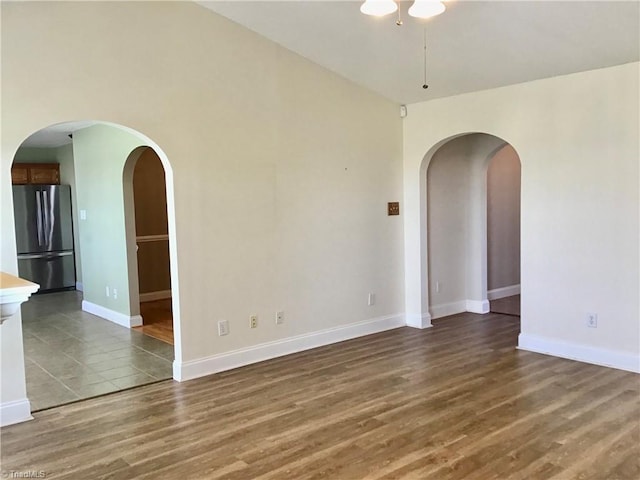 unfurnished room with arched walkways, dark wood finished floors, and baseboards