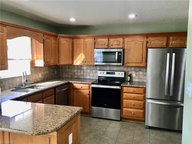 kitchen featuring light stone counters, stainless steel appliances, a sink, tile patterned floors, and brown cabinetry