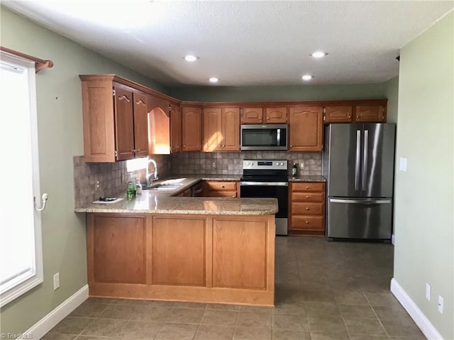 kitchen with decorative backsplash, appliances with stainless steel finishes, brown cabinets, a peninsula, and a sink