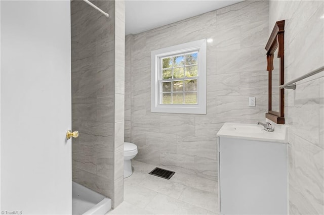 bathroom featuring vanity, toilet, a tile shower, and tile walls