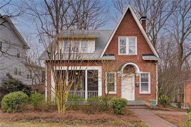 tudor house featuring brick siding, roof with shingles, and a chimney