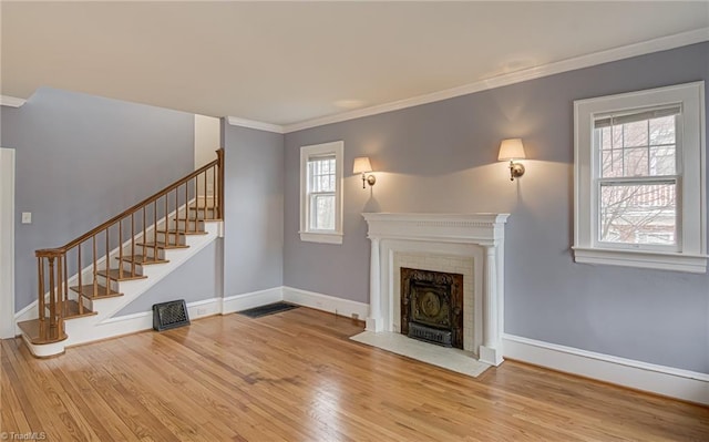 unfurnished living room with a fireplace with flush hearth, ornamental molding, wood finished floors, baseboards, and stairs