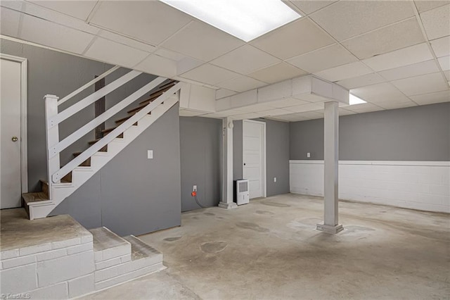 finished below grade area featuring a drop ceiling, concrete block wall, and stairs