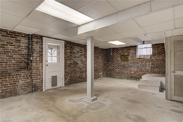 below grade area featuring a paneled ceiling and brick wall