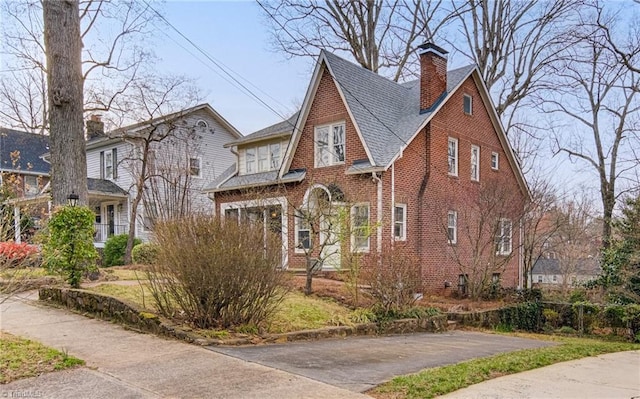 tudor house featuring a chimney, brick siding, and a shingled roof