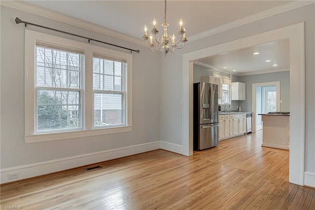 unfurnished dining area featuring visible vents, crown molding, light wood-type flooring, an inviting chandelier, and a sink