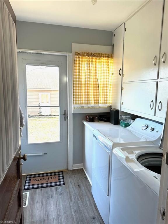 clothes washing area featuring independent washer and dryer, light hardwood / wood-style flooring, and cabinets