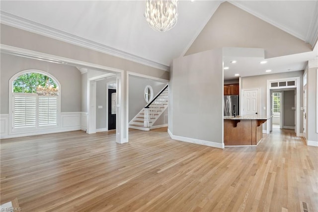 unfurnished living room featuring a chandelier, stairs, light wood-style flooring, a wainscoted wall, and high vaulted ceiling