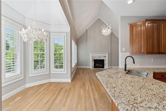 kitchen featuring a chandelier, a sink, healthy amount of natural light, light stone countertops, and lofted ceiling