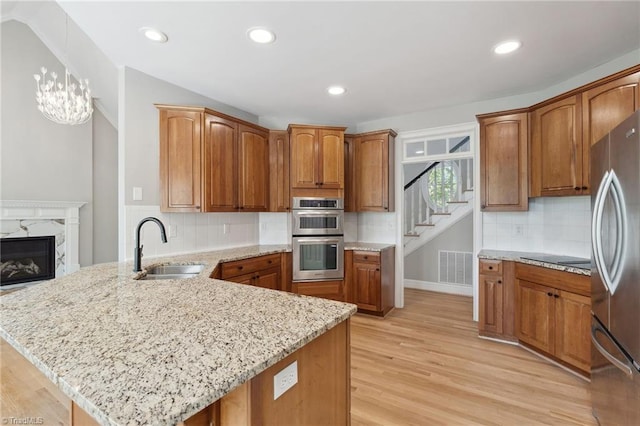 kitchen featuring appliances with stainless steel finishes, a sink, a peninsula, light wood finished floors, and light stone counters