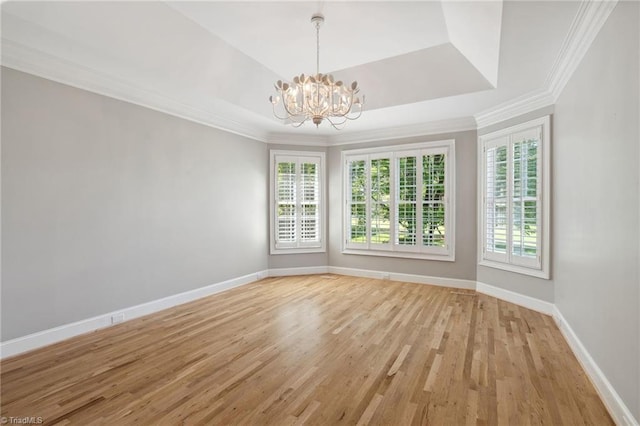 spare room featuring ornamental molding, light wood-style flooring, a chandelier, baseboards, and a tray ceiling