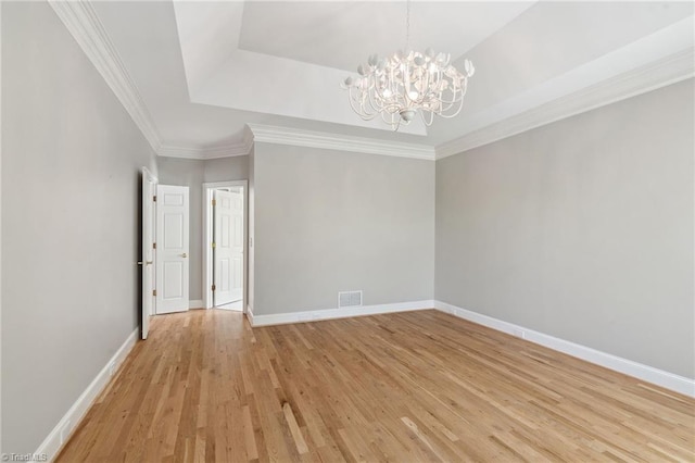 unfurnished room with a tray ceiling, a chandelier, light wood-style floors, baseboards, and ornamental molding