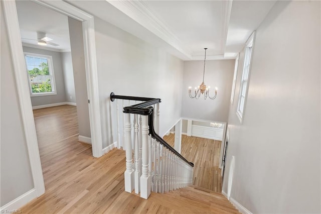 staircase with wood finished floors, ornamental molding, a chandelier, baseboards, and a raised ceiling