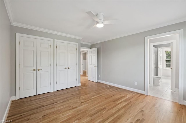 unfurnished bedroom with multiple closets, light wood-type flooring, ornamental molding, baseboards, and ensuite bath