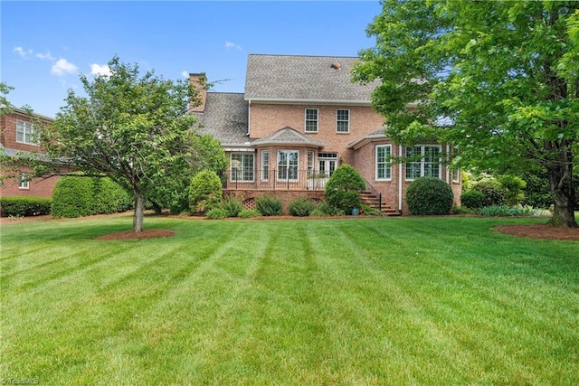 view of front facade featuring a front lawn, a chimney, brick siding, and stairs