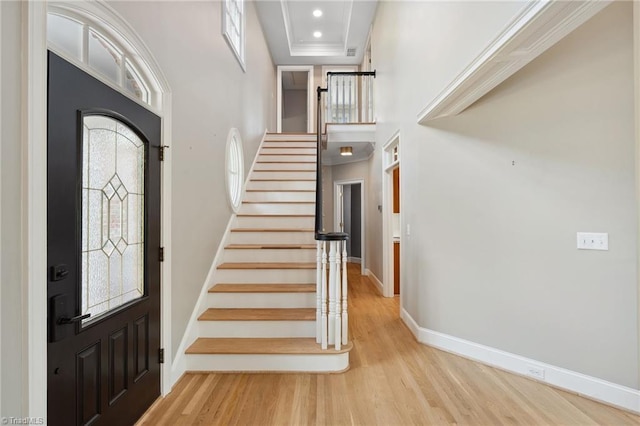 foyer entrance with a towering ceiling, baseboards, wood finished floors, stairway, and ornamental molding