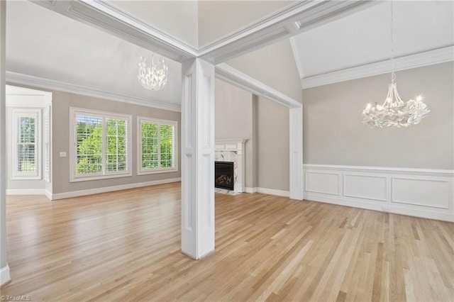 unfurnished living room featuring a chandelier, vaulted ceiling, ornamental molding, light wood-style floors, and a premium fireplace