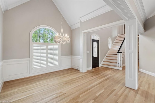 foyer entrance with a chandelier, stairs, wainscoting, light wood-style floors, and high vaulted ceiling