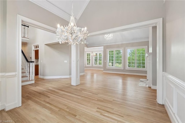 unfurnished dining area featuring a chandelier, ornamental molding, light wood-type flooring, stairway, and a decorative wall