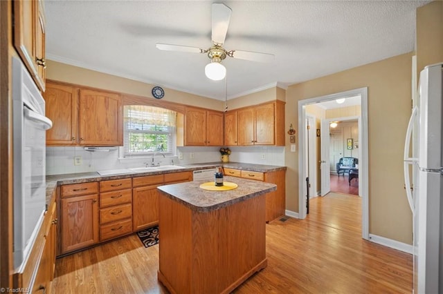 kitchen featuring light wood-type flooring, white appliances, a center island, and a sink