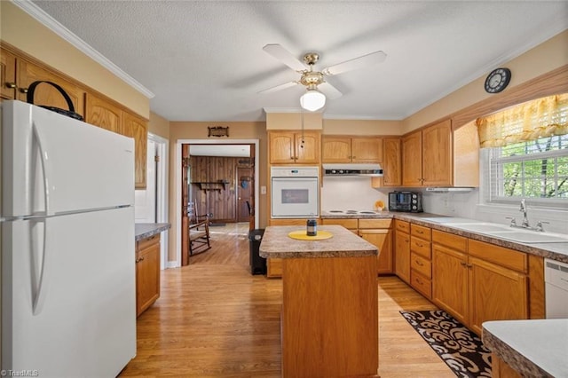 kitchen featuring a sink, light wood-style floors, a kitchen island, white appliances, and a ceiling fan