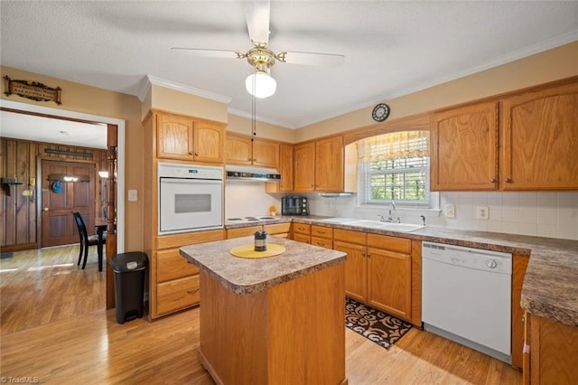 kitchen with light wood-style floors, white appliances, a kitchen island, and a sink