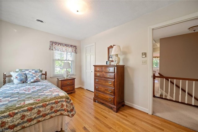 bedroom featuring baseboards, light wood-type flooring, visible vents, and a textured ceiling