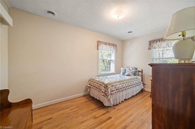 bedroom with baseboards, visible vents, multiple windows, and light wood-style flooring