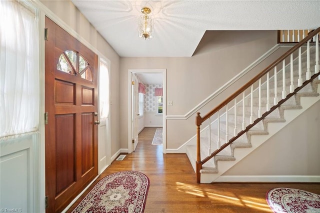 foyer with baseboards, visible vents, wood finished floors, and stairs