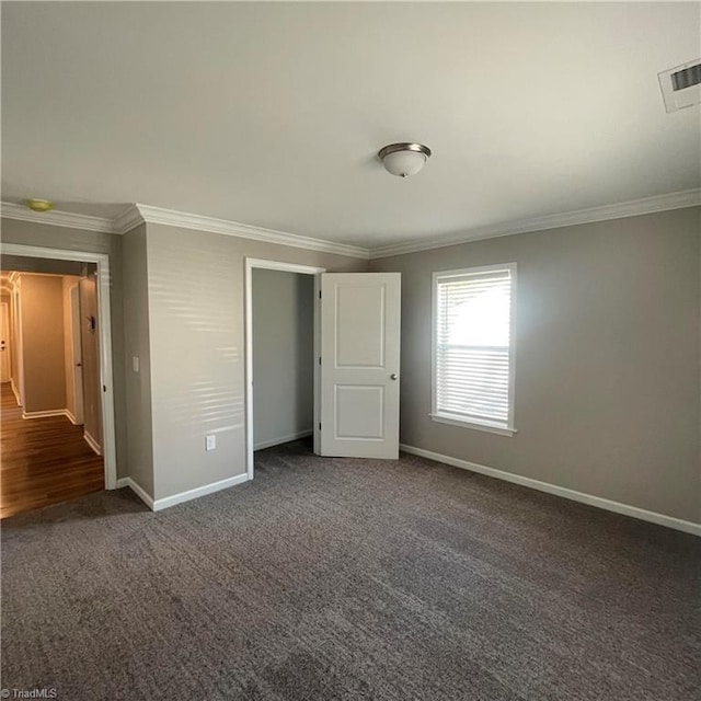 unfurnished bedroom with a closet, ornamental molding, and dark colored carpet